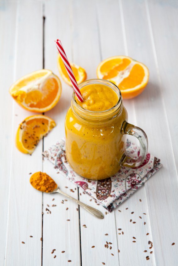 Smoothie surrounded by oranges and turmeric